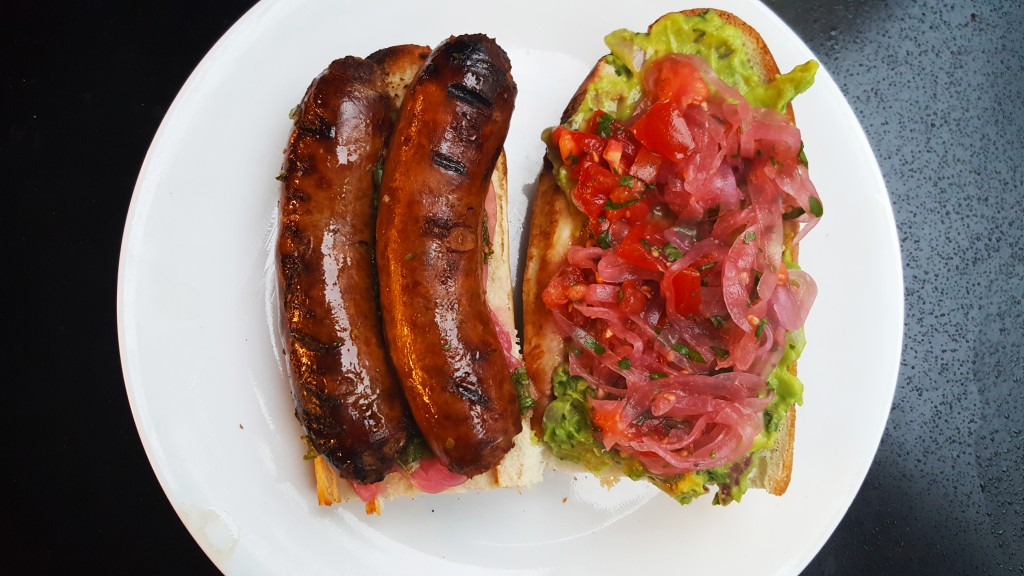 Homemade Argentine chorizo with onion curtido, chimichurri, guacamole, and tomato/onion curtido on baguette