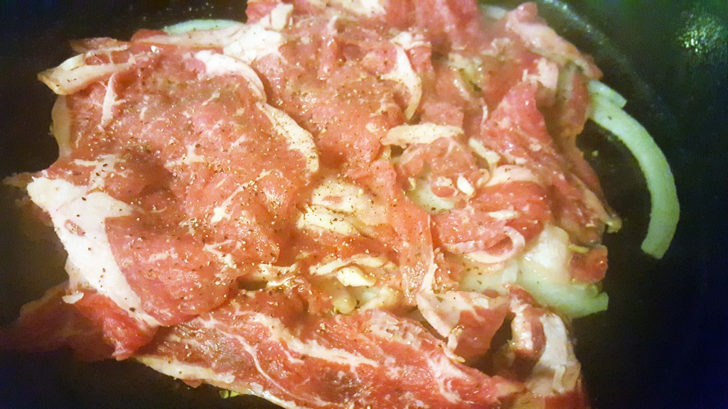 Seasoned steak and onions in the skillet