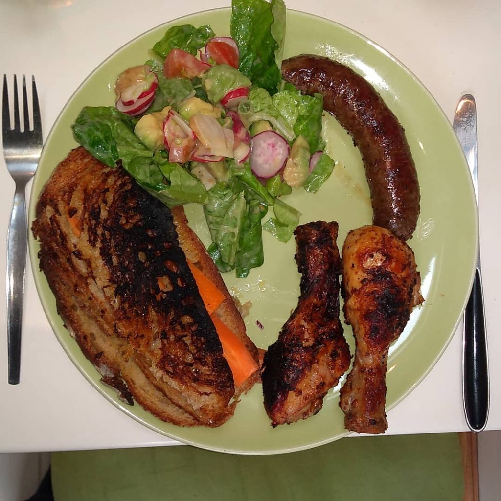 A plate of grilled sausage, chicken portions, green salad, and a grilled sandwich.